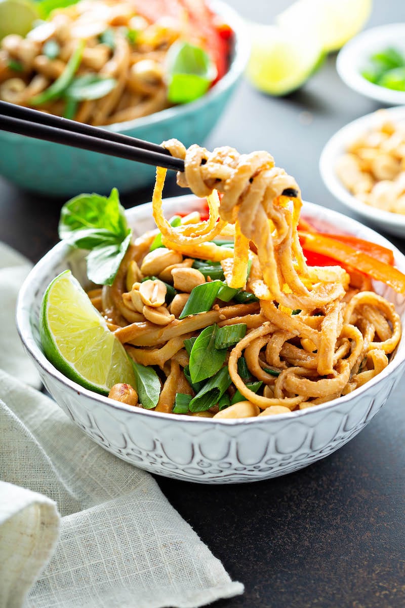 Spicy peanut noodles being picked up with chopsticks.