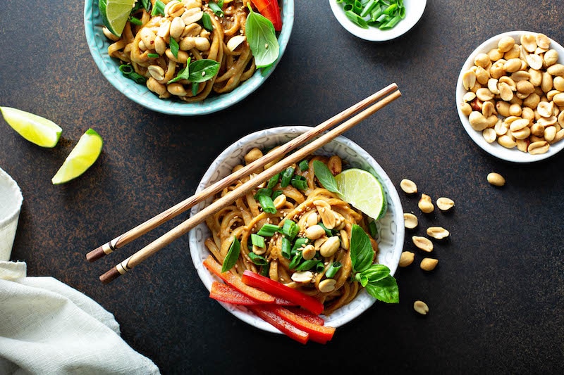 Spicy peanut noodles with chopped cilantro, peanuts, green onions, and a lime wedge.