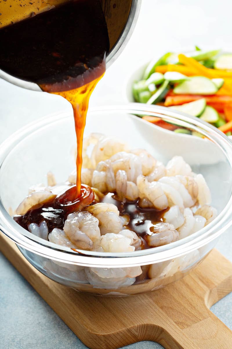 Homemade teriyaki sauce being poured over raw shrimp.