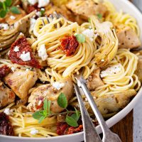 Pasta swirled in a plate with chicken, artichokes, sun dried tomatoes and goat cheese.