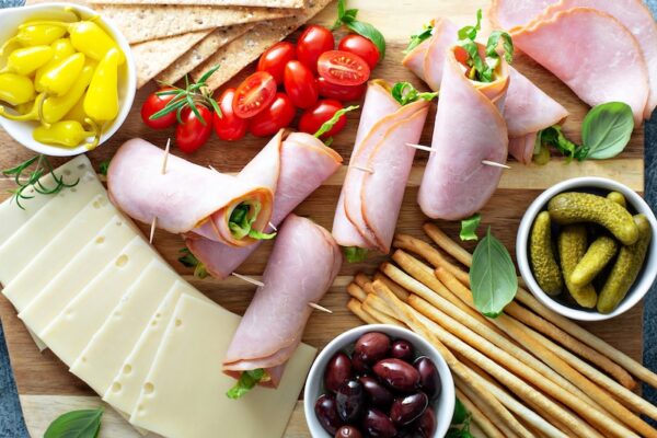 Ham Roll Ups on a platter with cheese, olives, tomatoes and more. 