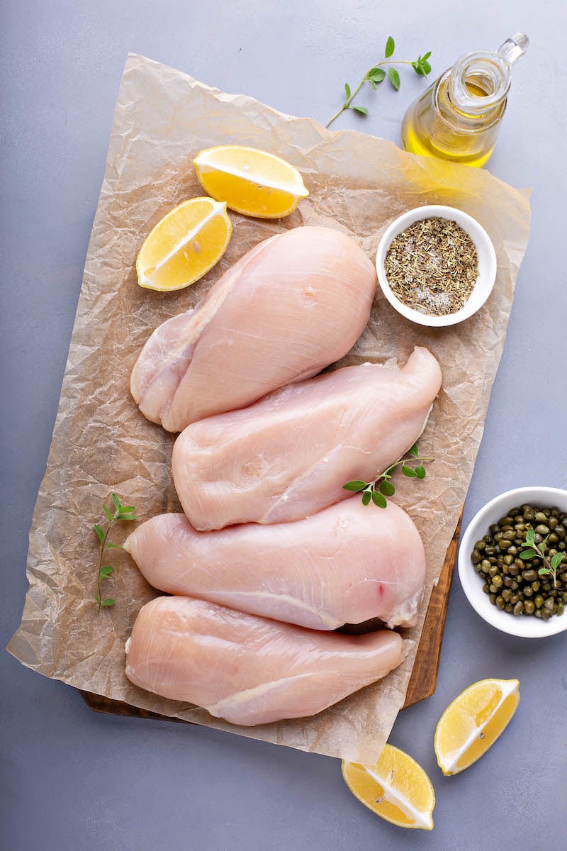 Chicken breasts on parchment paper with herbs and lemons and olive oil. 