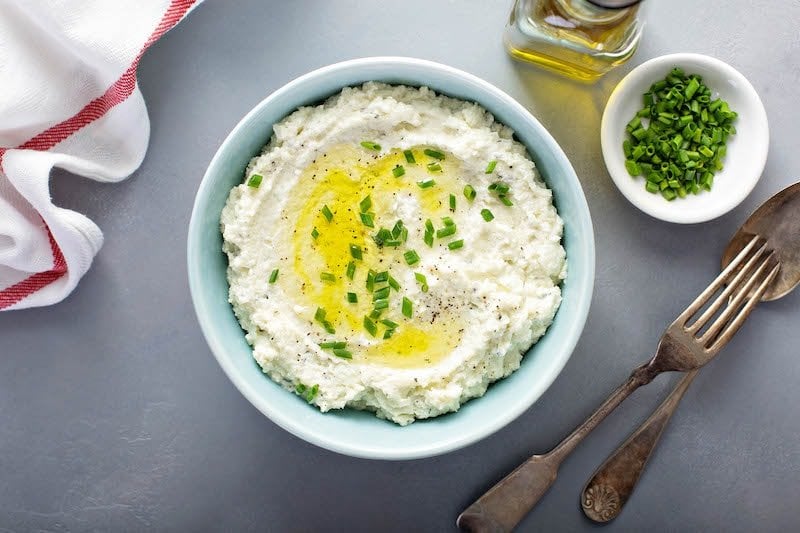 Cauliflower mash in a blue bowl with oil on top and chives.