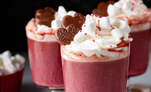 Red Velvet Hot Chocolate with marshmallow whipped cream swirled on top with marshmallows, sprinkles and chocolate hearts for garnish.