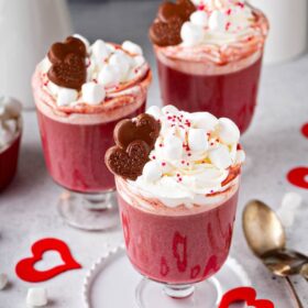 Three Red Velvet Hot Chocolates with marshmallow whipped cream and chocolate hearts on top.