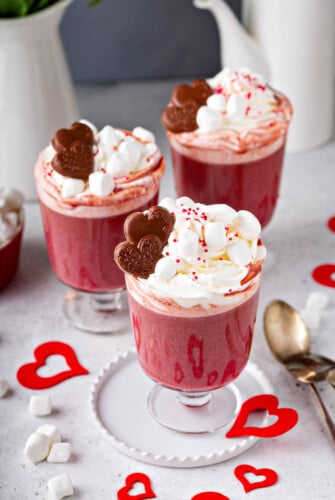 Three Red Velvet Hot Chocolates with marshmallow whipped cream and chocolate hearts on top.