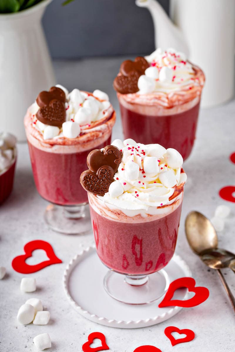 Three Red Velvet Hot Chocolates with marshmallow whipped cream and chocolate hearts on top. 