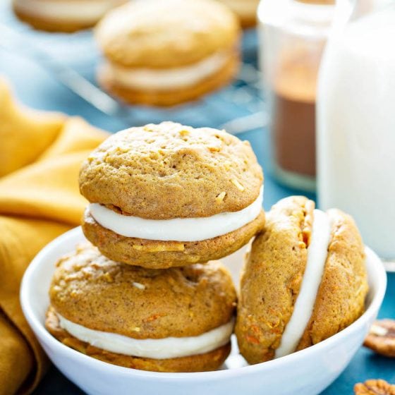 Carrot Cake Whoopie PIes stacked in a bowl with a glass of milk.