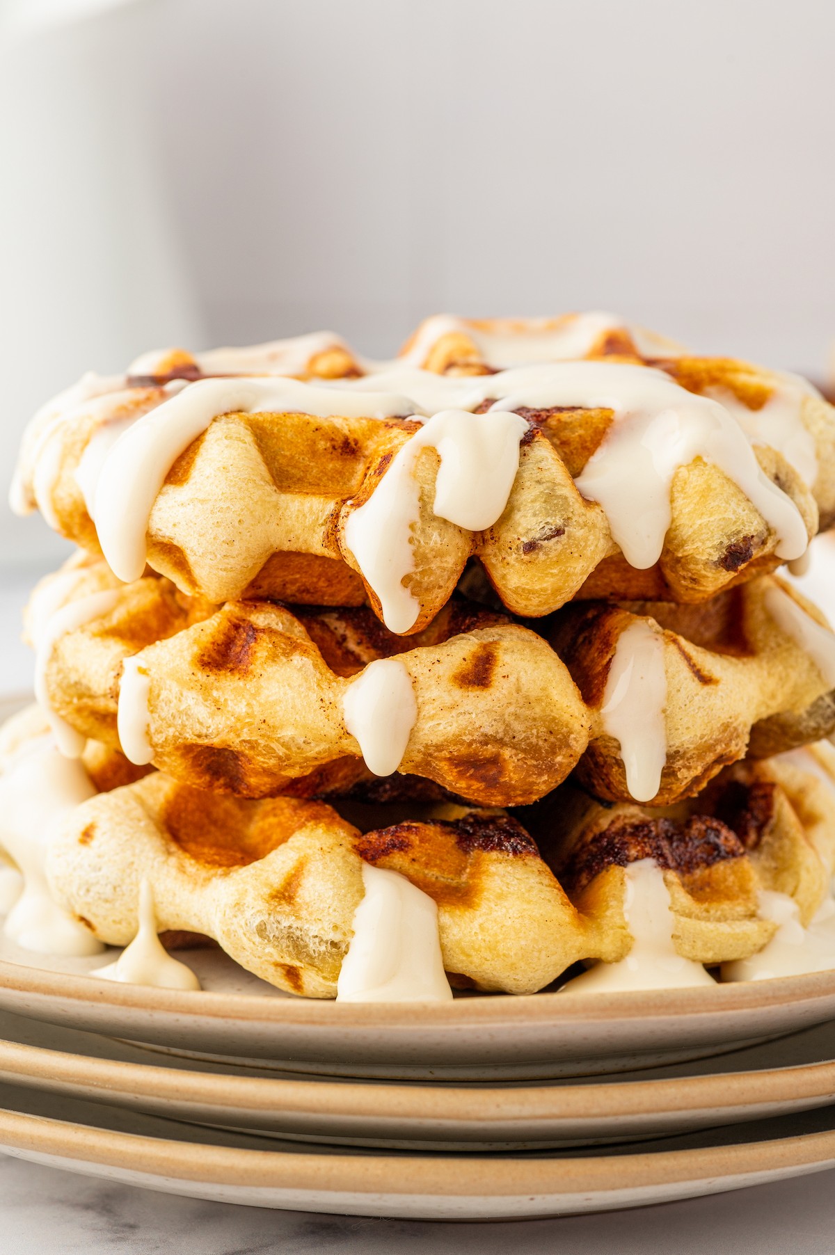 Three cinnamon roll waffles on a plate, with cream cheese maple syrup poured over.