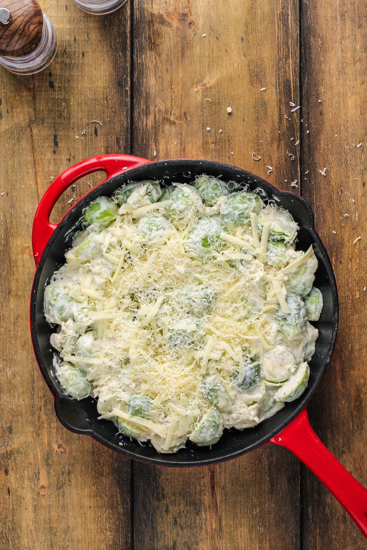 Creamy brussel sprouts in a cast-iron skillet with cheese sprinkled on top.