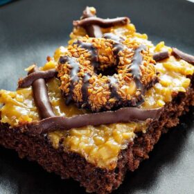 This Samoa Cookies Sheet Cake includes a rich chocolate sheet cake base, a layer of caramel coconut frosting, dark chocolate drizzle and samoa cookies on top! #SamoaCookies #Chocolate #SheetCake #Cake #ChocolateSheetCake #GirlScoutCookies #Dessert