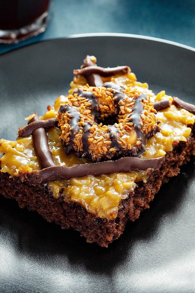 Piece of Samoa Cookies Sheet Cake topped with Samoa Girl Scout Cookie set in a black plate