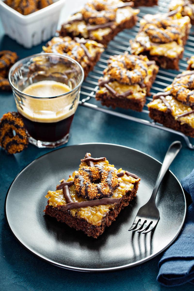 Samoa cookies on top of sheet cake on a plate.