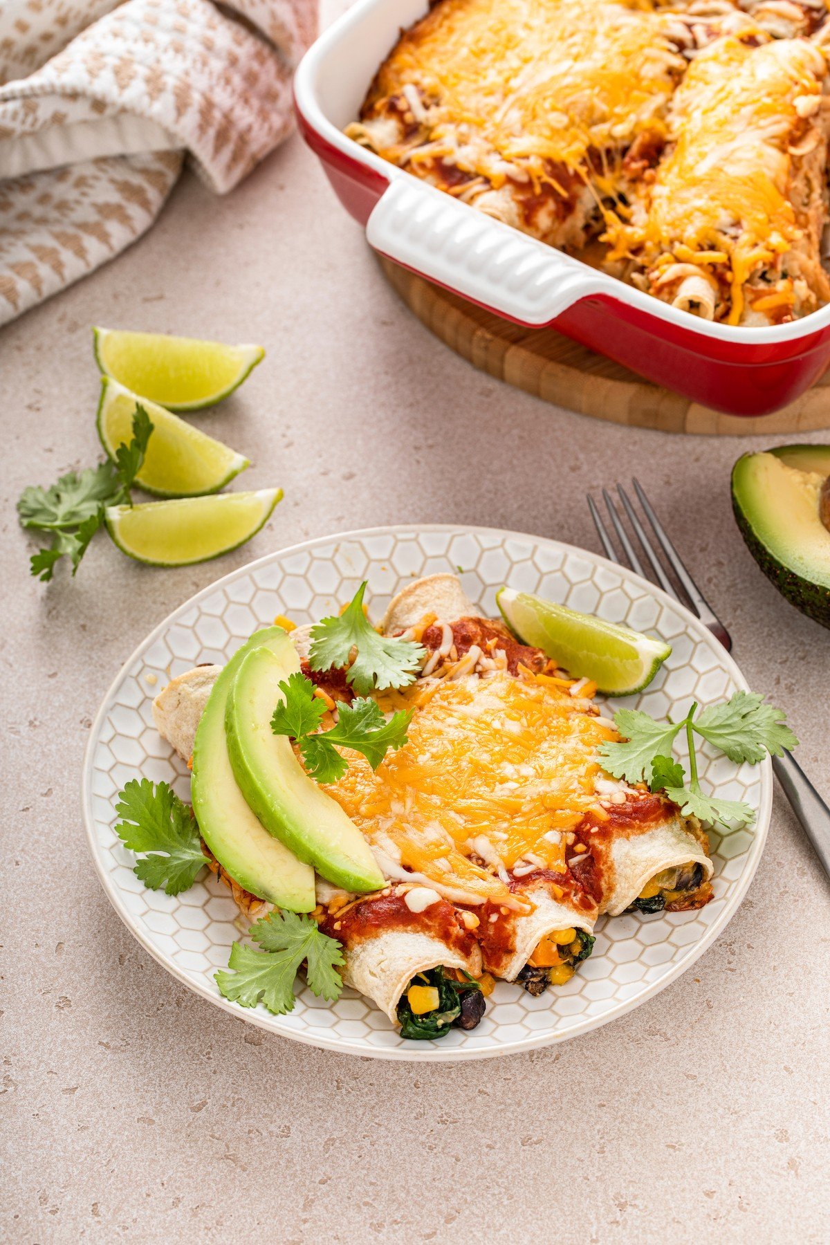 Three vegetable enchiladas on a plate with avocado slices