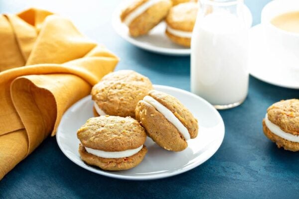 Carrot Cake Whoopie Pies on a plate with a glass of milk. 