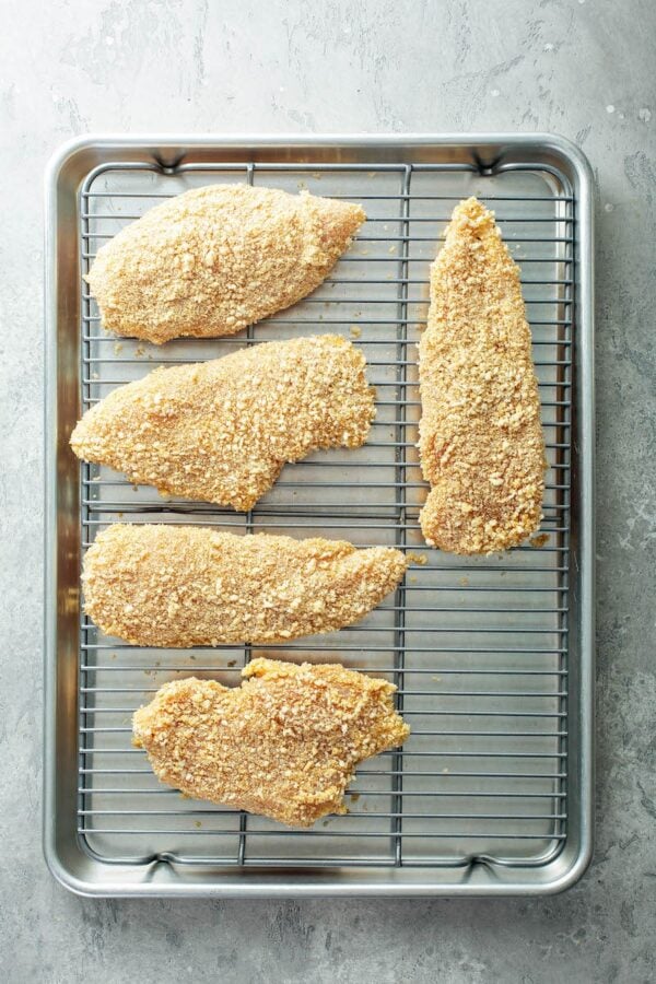 Chicken breasts on a cooling rack on a cookie sheet to make oven fried chicken.