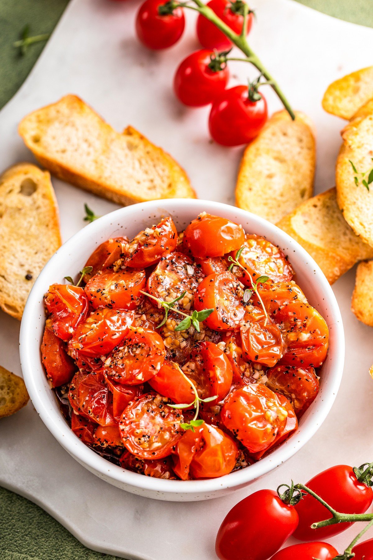 Bowl of roasted cherry tomatoes with crostinis on the side.