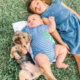 Two kids and a dog laying in grass.