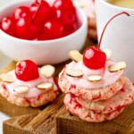 Cherry Almond Sugar Cookies stacked together with maraschino cherries on a cutting board.