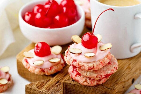 Cherry Almond Sugar Cookies stacked together with maraschino cherries on a cutting board. 