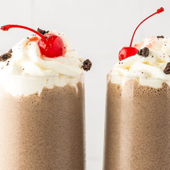 Two milkshakes topped with cherries.