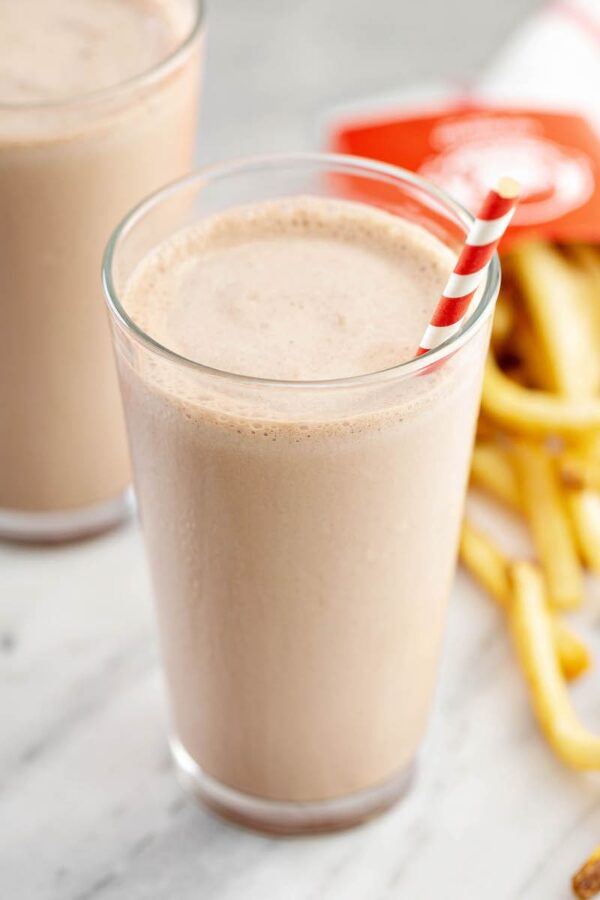 Homemade chocolate frosty in a glass with a straw and fries.