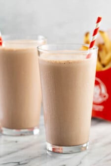 Two copycat wendy’s chocolate frostys in glasses with fries.