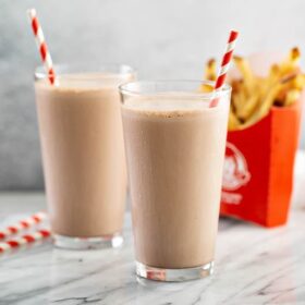 Two copycat wendy’s chocolate frostys in glasses with fries.