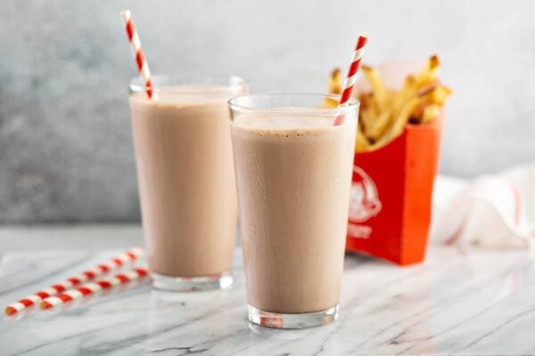 Two copycat wendy’s chocolate frostys in glasses with fries.