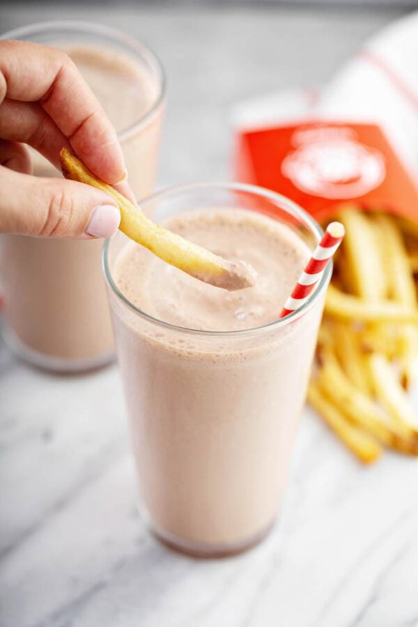 Homemade chocolate frosty in a glass with fries being dipped into it. 