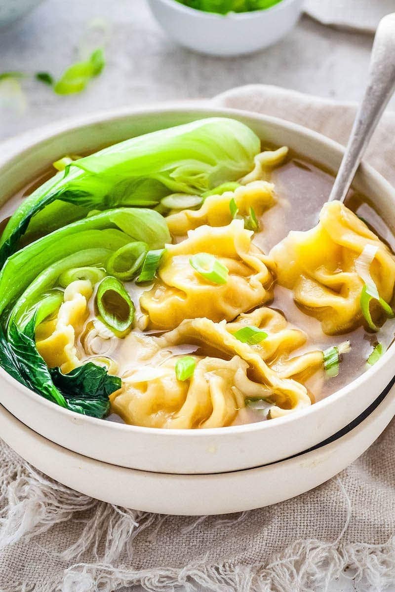 Wonton Soup in a bowl with bok choy and a spoon.