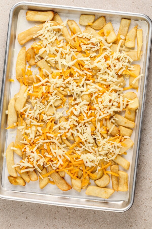 Fries sprinkled with cheese on a baking sheet.