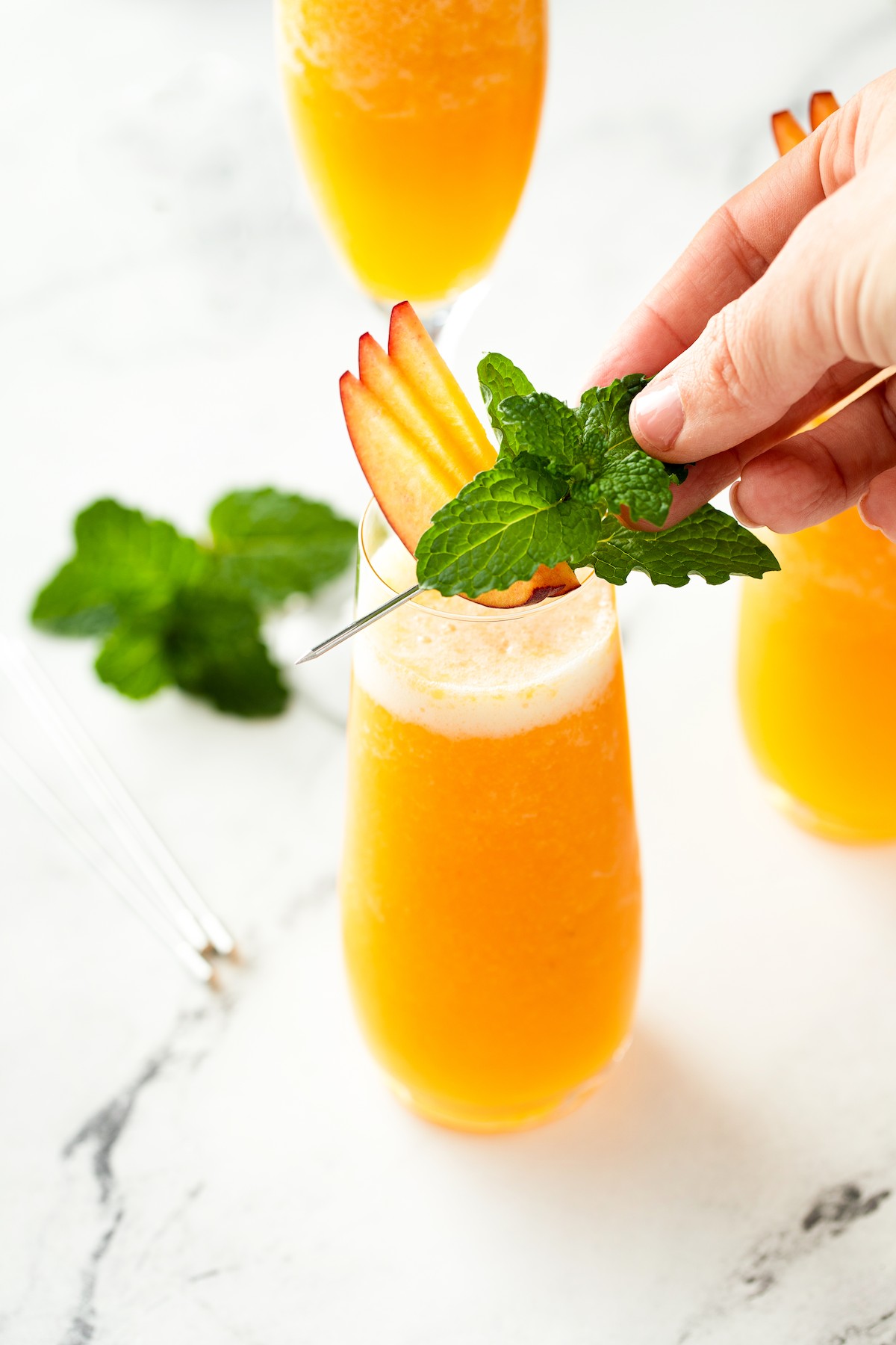 Garnishing a drink with thin slices of peach and a sprig of mint.