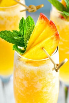 Up close image of peach bellini with fresh peaches and mint on top.