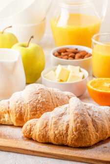 brunch recipe table filled with juices, fruits and croissants.