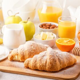 brunch recipe table filled with juices, fruits and croissants.
