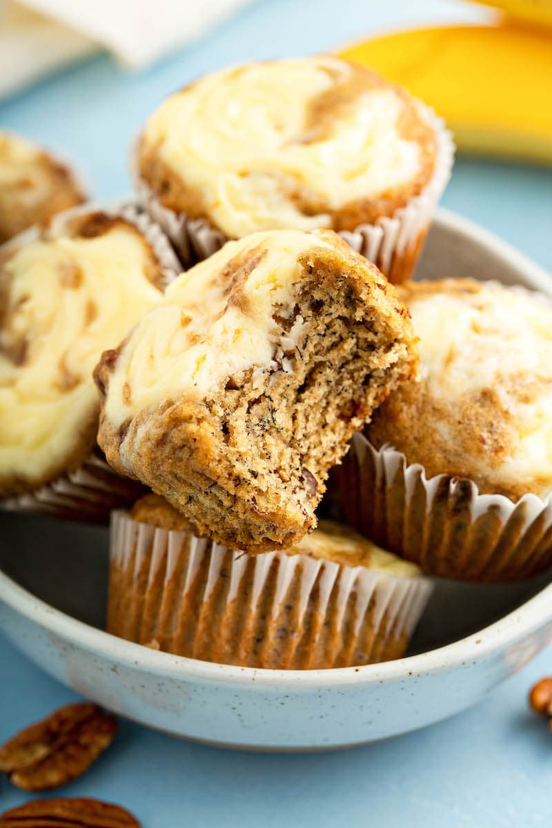 Banana Cream Cheese Muffins in a bowl with a bite taken out of one.