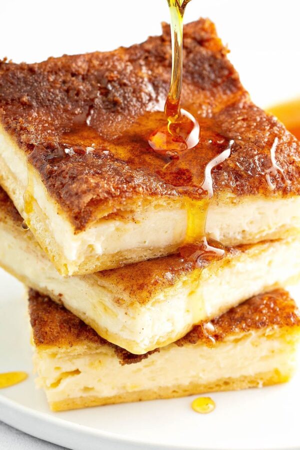 Sopapilla Cheesecake stacked on top of each other with a drizzle of honey.