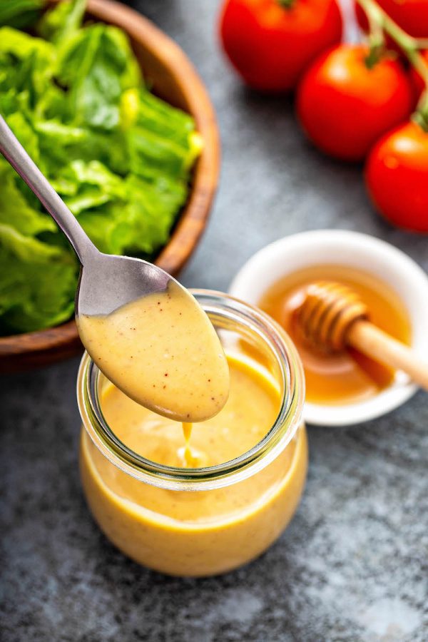 Honey Mustard sauce in a glass jar with a spoon scooping some out.