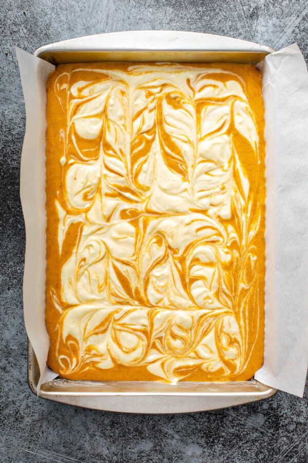 Unbaked pumpkin bars with cheesecake swirled through them in a baking pan.