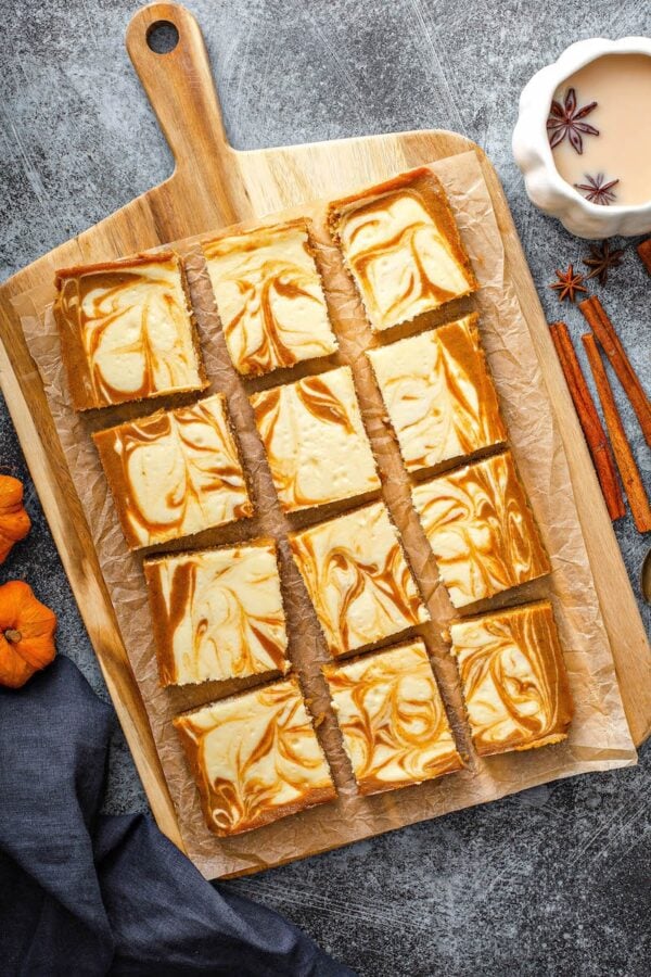 Overhead image of pumpkin bars with cheesecake swirled through them on parchment paper. 