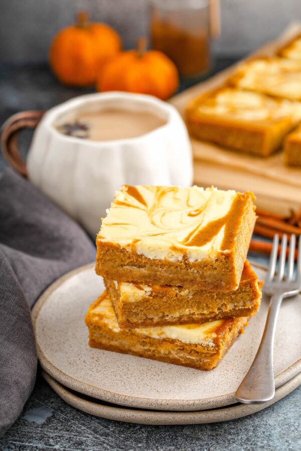 Stacked pumpkin cheesecake bars on a plate.