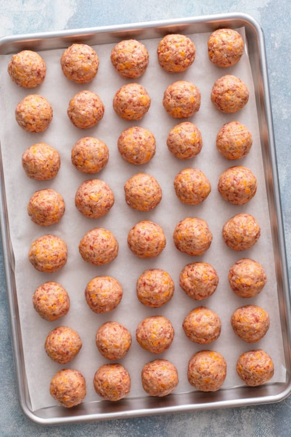 Uncooked sausage balls are placed on a baking sheet.