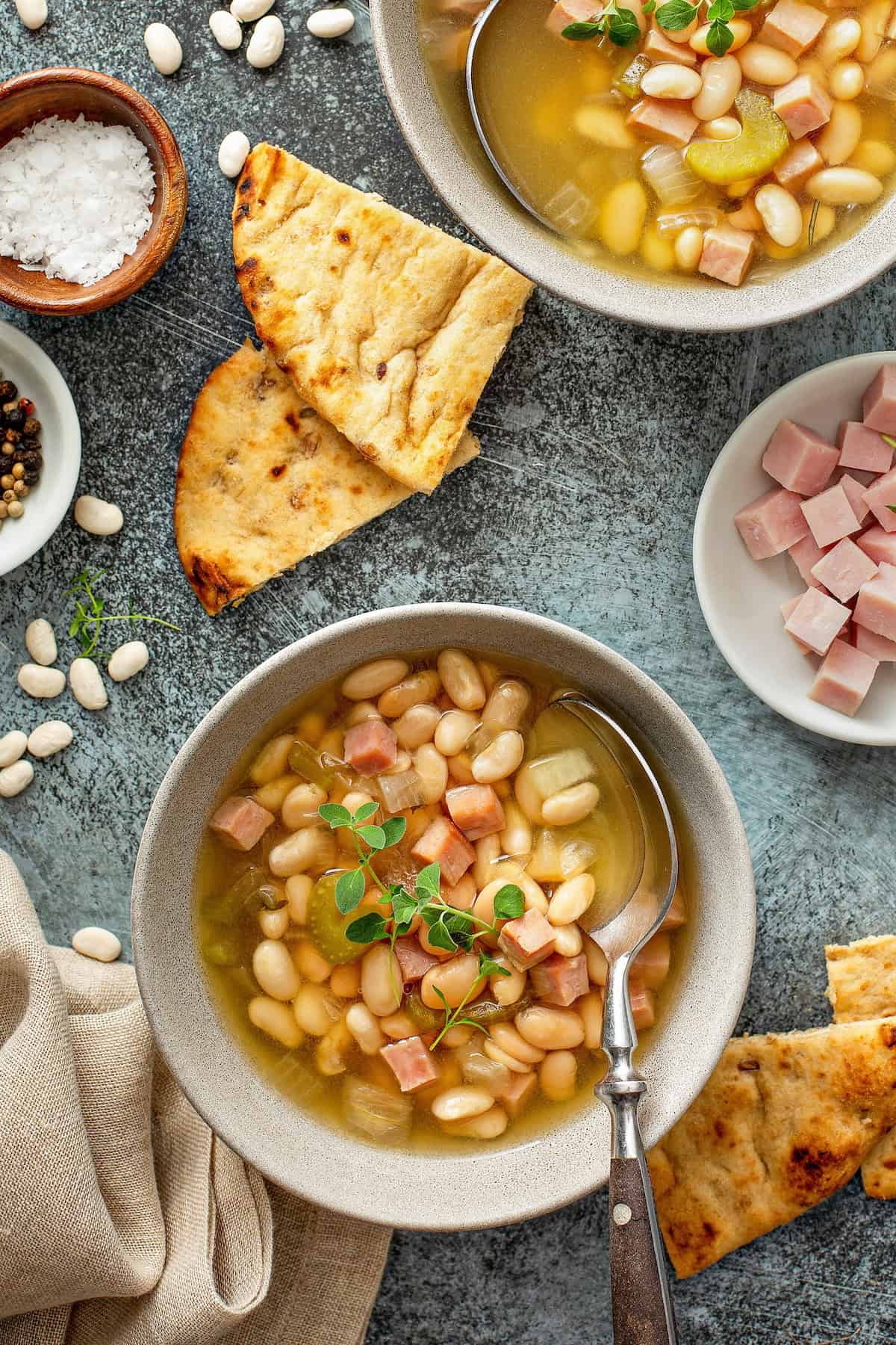 Two pieces of bread are placed next to bowl of crockpot ham and bean soup.