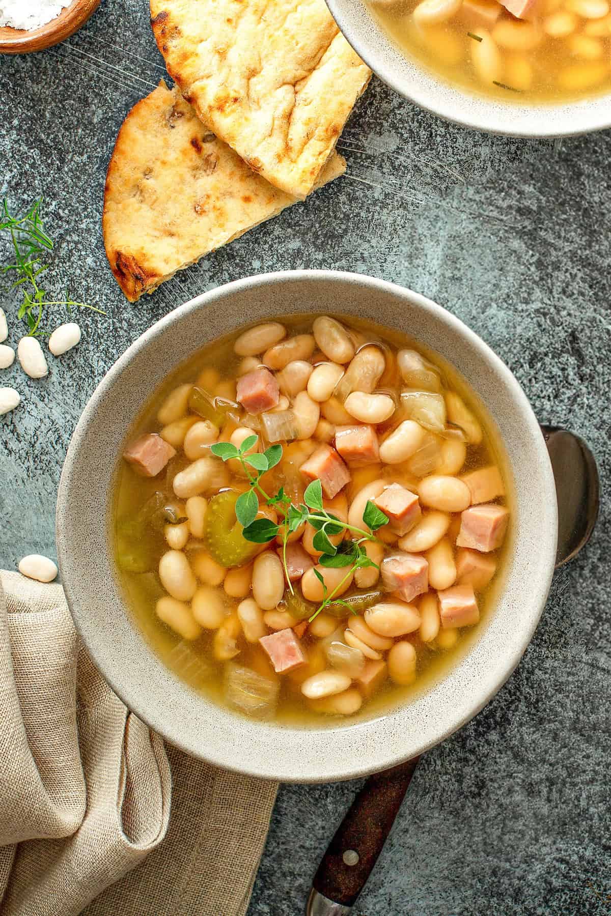 A bowl of ham and bean soup is placed next to slices of bread.