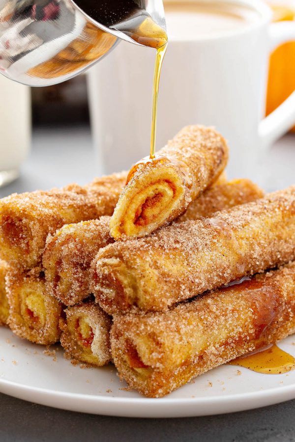 Pumpkin French Toast Roll-ups on a white plate with syrup being drizzled on top.