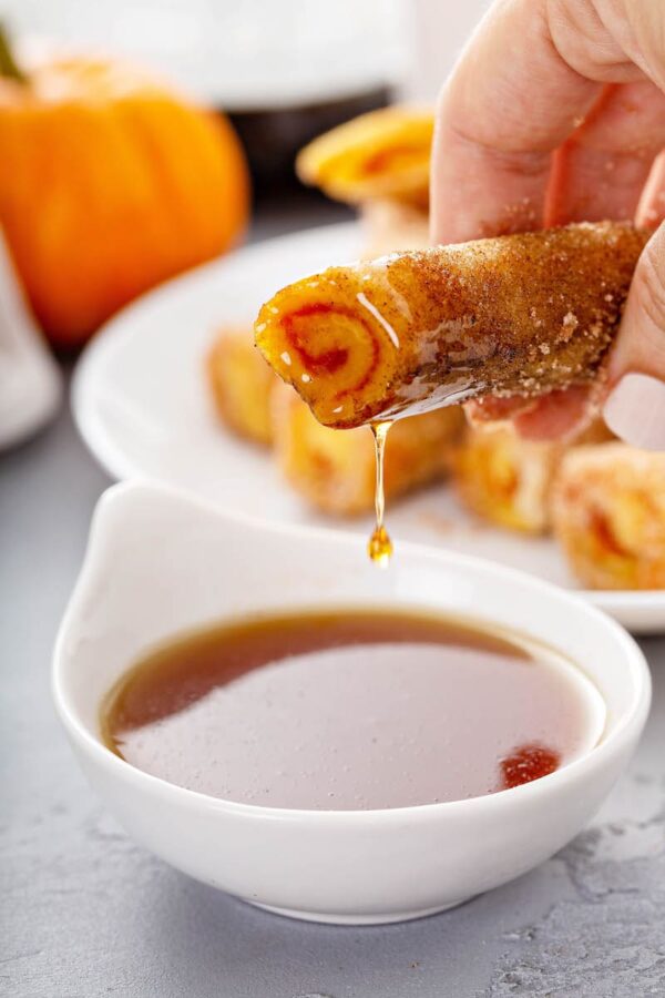 Pumpkin French Toast Roll-ups being dunked in syrup.