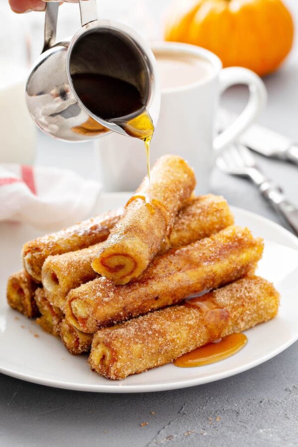 Pumpkin French Toast Roll-Ups stacked on a plate with maple syrup.