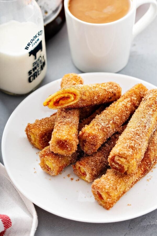 Pumpkin French Toast Roll-Ups on a white plate with a cup of milk.