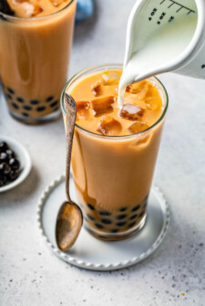 Bubble tea in a glass jar with tapioca pearls in the bottom and cream being poured on top.
